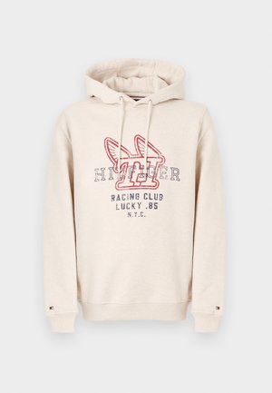 Beige kapuutsiga dressipluus, mille esiosas on tekst "Tommy Hilfiger Racing Club Lucky .85 NYC" ja tiivulise "H" logo punases ja tumesinises värvitoonis, nööriga kapuuts ja soonikud varrukate otsas.