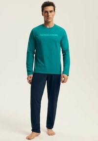 Turkusowa koszula z długim rękawem z napisem "HENDERSON" w jaśniejszym odcieniu turkusu, zestawiona z ciemnogranatowymi spodniami, obie uszyte z miękkiego materiału.