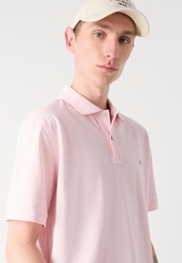 Polo shirt rose clair avec un col classique, des manches courtes et un petit logo sur la poitrine. Fabriqué en tissu doux et respirant.