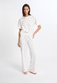 Conjunto de pijama blanco que incluye una camiseta de manga corta y pantalones sueltos con un patrón floral repetido en rojo y verde. Tejido suave y liviano.