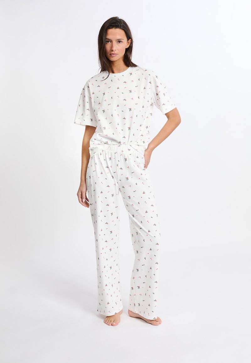 Conjunto de pijama blanco que incluye una camiseta de manga corta y pantalones sueltos con un patrón floral repetido en rojo y verde. Tejido suave y liviano.