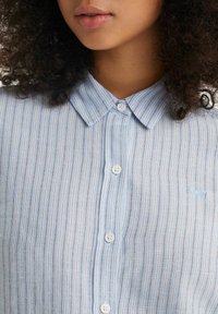 Jasnoniebieska koszula w paski z kołnierzykiem button-down, z białymi guzikami i małą naszywką z logo. Miękka tkanina o teksturowanym wykończeniu.