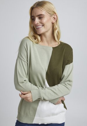 Pull en tricot vert et blanc avec un col rond et des épaules tombantes, présentant un design en blocs de couleurs et des poignets et un ourlet côtelés.