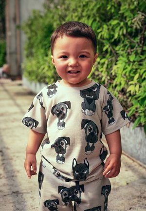 Beige Outfit mit schwarzen und grauen Cartoon-Hundedrucken. Das Shirt hat kurze Ärmel, und die Hose ist ähnlich gestaltet mit einem elastischen Bund.