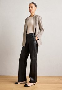 Blazer a pied de poule con vestibilità su misura, abbinato a pantaloni in pelle nera a vita alta e ballerine beige con dettagli neri.