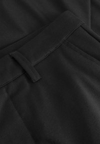 Svart tyg med en slät textur, med ett bälte i midjan och diskreta fickor. Designen är elegant med rena linjer och minimal detaljering.