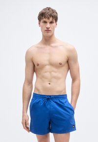 Μπλε μαγιό σορτς με ελαστική μέση και κορδόνι. Διαθέτει πλαϊνές τσέπες και ένα μικρό πλακάκι με λογότυπο στο αριστερό τελείωμα. Λεπτή υφή.