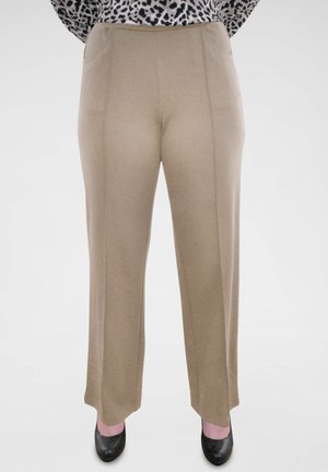 Pantalons larges beiges avec une texture lisse, dotés de poches avant et de coutures verticales. Associés à des chaussures noires.