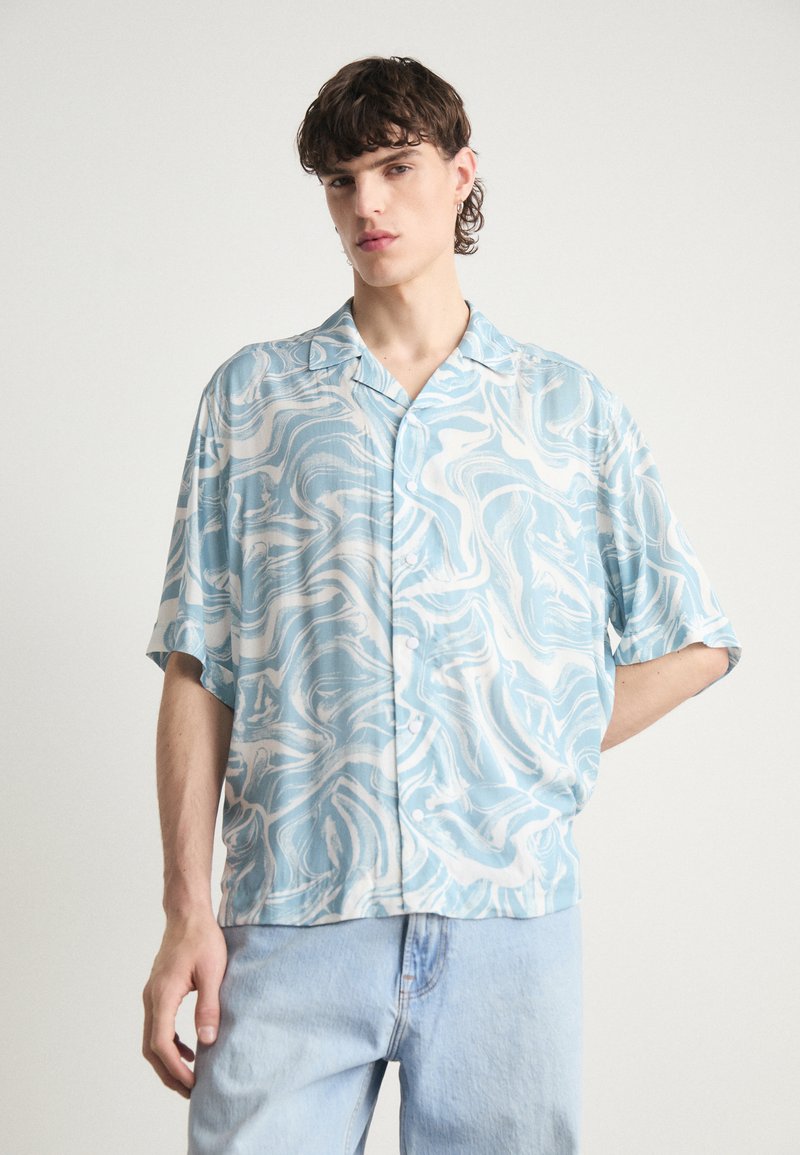 Camicia a maniche corte con bottoni di colore azzurro chiaro e motivo marmorizzato bianco, realizzata in tessuto morbido. Vestibilità casual con colletto da campeggio e maniche comode.