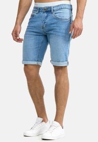 Shorts in denim azzurro chiaro con orlo arrotolato, caratterizzati da un classico design a cinque tasche e chiusura con bottone. Abbinati a sneakers bianche.