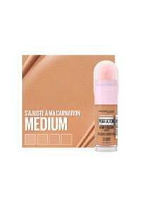 Maybelline maquillage 4-en-1 Glow dans un stick rétractable avec un applicateur fluffy rose, mettant en avant une teinte beige moyenne sur un fond pêche.