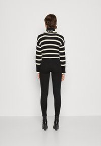 Czarny i biały sweter z golfem w paski, krótki fason, prążkowana faktura, w połączeniu z czarnymi rurkami i czarnymi botkami na obcasie.