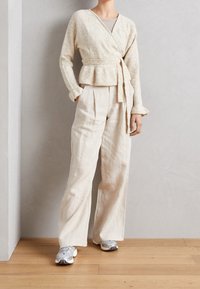 Cream wrap cardigan with textured knit, belted waist, and long sleeves. Paired with light beige wide-leg linen pants and gray sneakers.