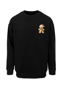 Sort sweatshirt med et peberkagemandsgrafik iført en rød julesløjfe på venstre brystområde. Lavet af blødt, tykt materiale.