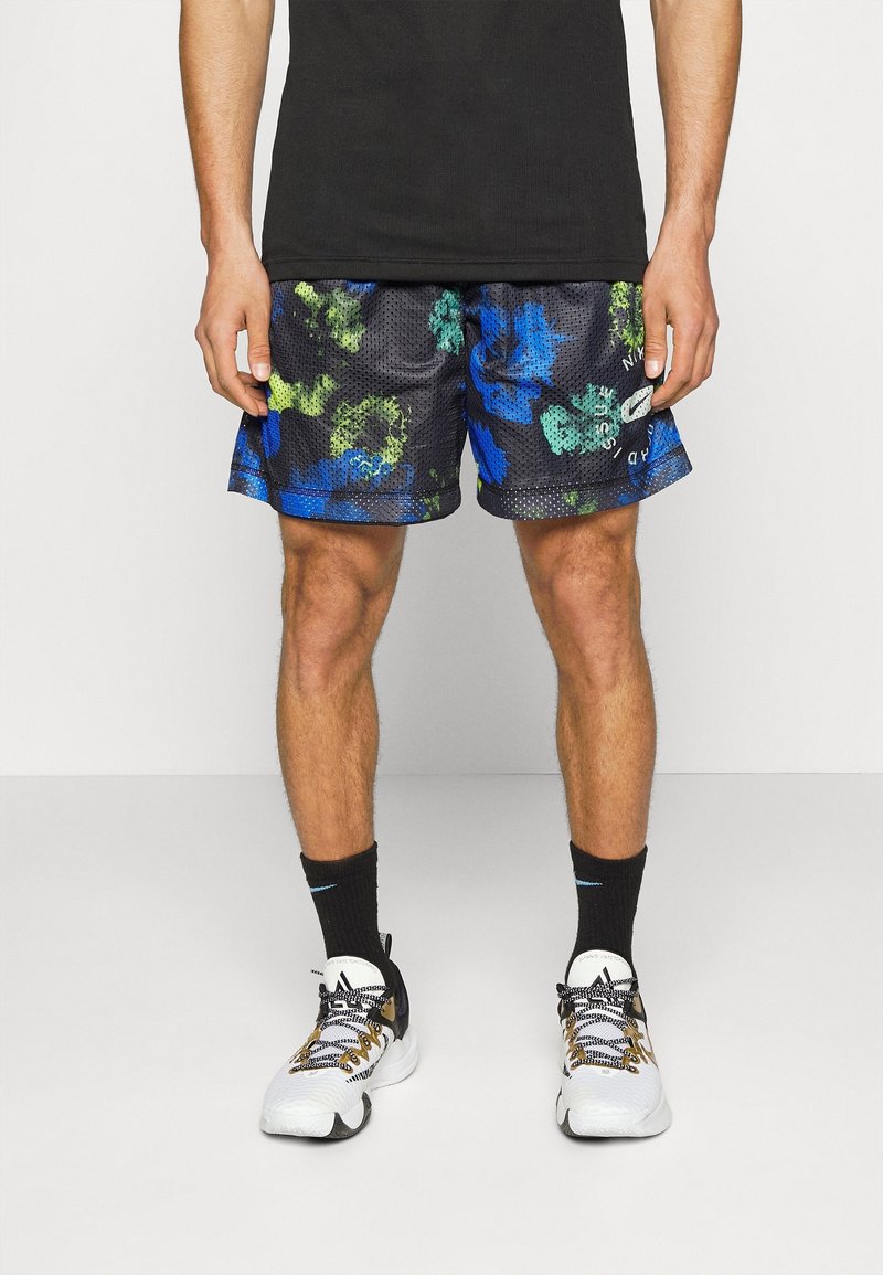 Shorts de sport noirs avec un motif floral en bleu et vert, en tissu en maille, taille élastique, associés à des chaussettes noires et des baskets blanches.