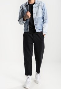 Lyseblå denimjakke med et falmet design, sort skjorte, løse sorte bukser og hvide sneakers. Ren, moderne stil uden mønstre.