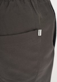 Dark green fabric shorts with an elastic waistband, featuring a side pocket and a small white label on the pocket seam.