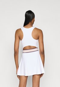 Rochie sport albă cu un corp ajustat, design de tip racerback și fustă evazată. Prezintă o secțiune decupată la spate și un cordon cu dungi.