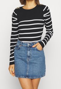 Schwarz-weißer gestreifter Langarmshirt mit gerippter Textur und goldenen Knopfakzenten, kombiniert mit einem blauen Denim-Minirock mit einer Vordertasche.