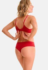 Ensemble de lingerie rouge composé d'un tissu doux et texturé. Le soutien-gorge a des bretelles réglables et une fermeture à crochet. Le slip a un design taille basse.