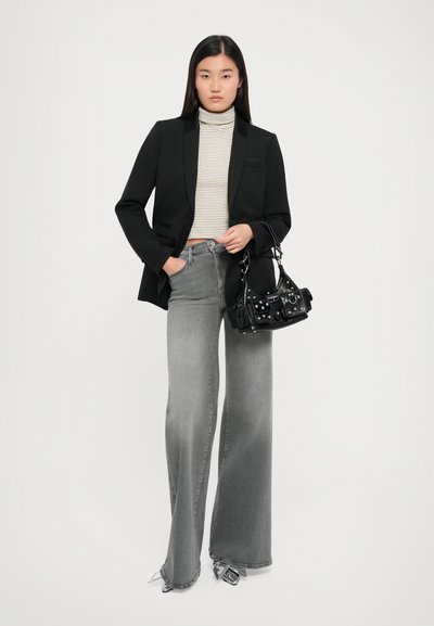 Black blazer over a striped turtleneck, paired with wide-legged grey jeans. Accessory: small black bag with metallic details.