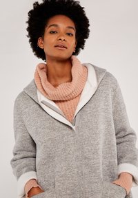 Grau zip-up Hoodie mit weißen Akzenten, ausgestattet mit einer weichen, strukturierten Oberfläche und großen Taschen. Darunter befindet sich ein pinkfarbener gestrickter Kragen.