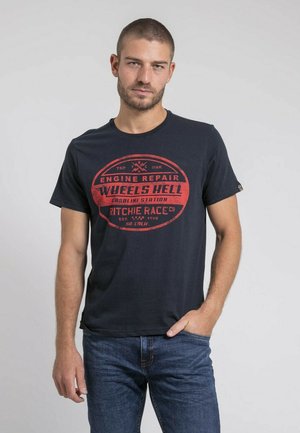 T-shirt en coton noir avec un col rond et des manches courtes, ornée d'un design graphique rouge avec du texte, associée à un jean en denim bleu.