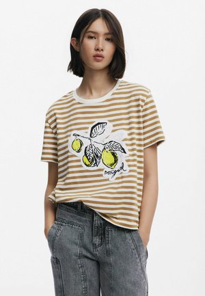 Una camiseta a rayas beige y blanca presenta un gráfico de limones verdes y hojas, con la palabra "desigual" impresa debajo. Manga corta, ajuste relajado.
