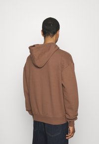 Brun huva sweatshirt med en avslappnad passform, mjuk textur och ribbade manschetter och fåll. Utsikt bakifrån utan synlig märkning.