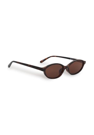 Lunettes de soleil ovales en écaille avec verres teintés marron et branches fines reposant sur une surface blanche.