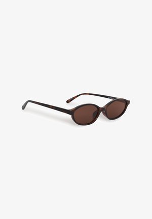 Lunettes de soleil ovales en écaille avec verres teintés marron et branches fines reposant sur une surface blanche.
