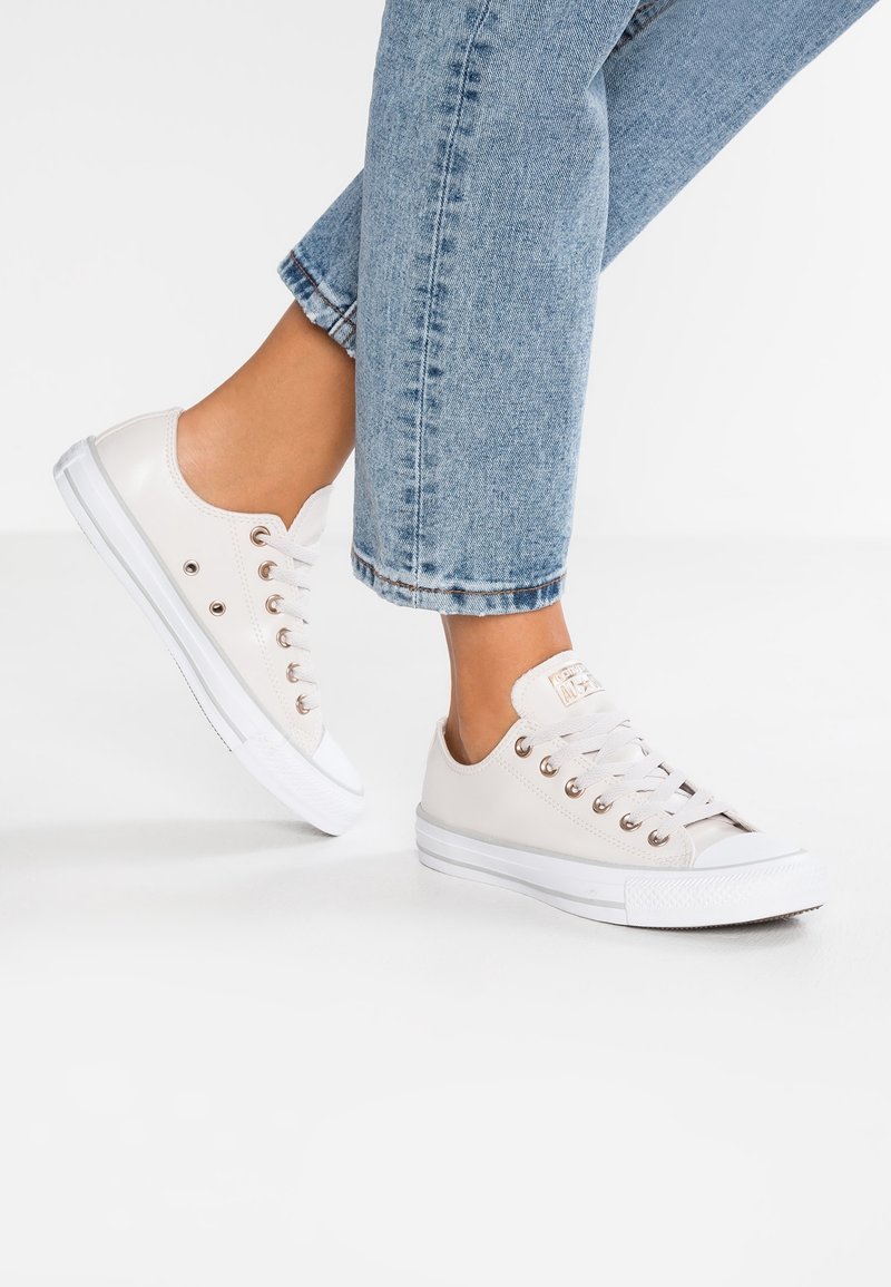 Canvas sneakers i off-white med metallöglor, vita gummisulor och en kontrasterande tåkappa; stylade med mönstrade ljusblå jeans.