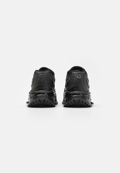 Black athletic shoes with a textured fabric upper, glossy accents, and a thick, ridged rubber sole. Features circular eyelets and branded details.