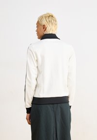 White sweatshirt with a black collar and cuffs, featuring black side stripes, paired with a black pinstripe skirt, smooth texture.