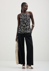 Top senza maniche nero con motivo floreale bianco, abbinato a pantaloni neri a gamba larga. Gli accessori includono una borsa intrecciata e sandali con tacco beige.