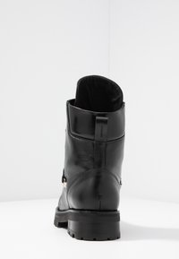 Bottine en cuir noir avec un bout rond, finition texturée et une semelle basse et robuste. Elle présente un détail zippé sur le côté et une boucle à l'arrière.