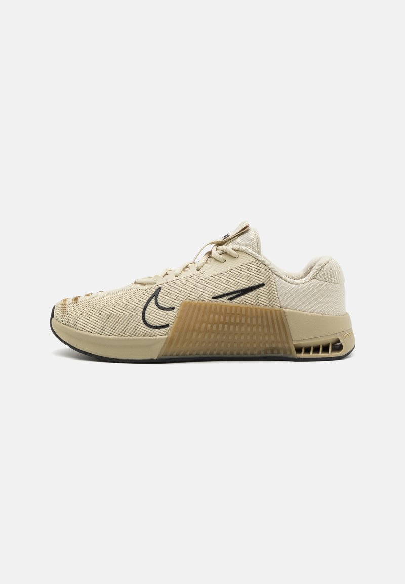 Light beige athletic shoe with mesh upper, black accents, textured heel, and rubber sole featuring a pronounced grid pattern.