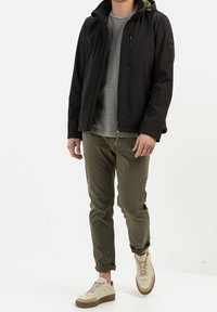 Schwarze Zip-Jacke mit Kapuze, graues T-Shirt, olivgrüne Hose und beigefarbene Sneaker mit braunen Akzenten. Einfaches Design, lässige Passform.
