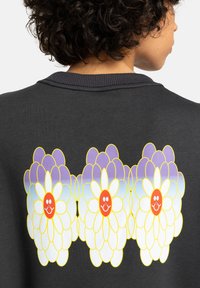 Zwarte sweatshirt met een grote afbeelding van drie gestileerde bloemen met witte bloemblaadjes, oranje centra en lavendelaccenten op de achterkant.
