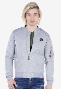 Lichtgrijze bomberjack met ritssluiting aan de voorkant, ribgebreide manchetten en onderrand. Bevat zijzakken en een mouwzak met hardwaredetails.