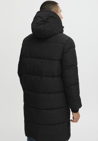 Sort polstret jakke med hætte, der har vandret kviltning og en længere silhuet. Stoffet ser glat og isoleret ud.