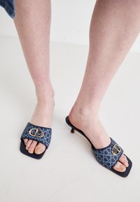 Mules avec une tige en tissu à motifs bleus, mettant en avant un détail de boucle dorée, un bout carré et un petit talon kitten.