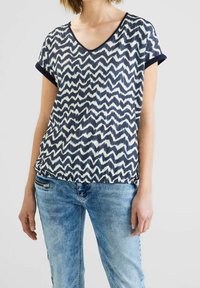 Haut à manches courtes bleu marine et blanc avec un col en V, associé à un jean en denim bleu clair avec un détail de poche zippée.