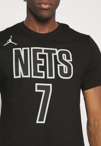 Černé bavlněné tričko s bílým potiskem "NETS" a "7", s malým logem Jumpman na levém rameni. Krátké rukávy, kulatý límec.