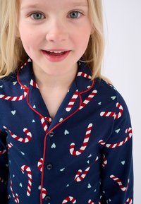Camisa de pijama azul marino con ribetes rojos, que presenta un motivo de bastones de caramelo en rojo y blanco, con pequeños corazones verde menta en una tela suave.