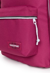 Rosa Eastpak-ryggsäck i texturerad tyg, med en framficka med dragkedja och en vit snodd, varumärkeslogotyp.