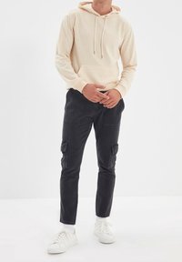 Beige mikina s kapucí a přední kapsou, zkombinovaná s černými cargo kalhotami se bočními kapsami a bílými teniskami. Jednoduchý, pohodlný design.
