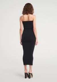 Abito midi nero aderente con design senza spalline e tessuto texturizzato, che presenta una silhouette fluida che si estende fino a metà polpaccio.