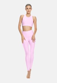 Světlý růžový sportovní set skládající se z sportovní podprsenky s vysokým výstřihem a elastických legín s vysokým pasem s hladkou, pružnou texturou, vhodný pro aktivní nošení.