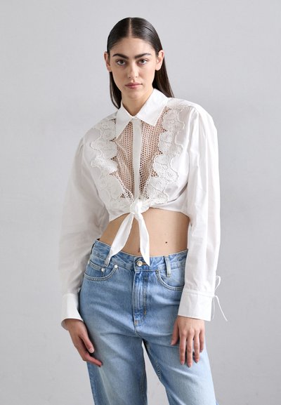 Vit avkortad blus med spetspaneldesign, knuten vid midjan, kombinerad med ljusblå högmidjade jeans.